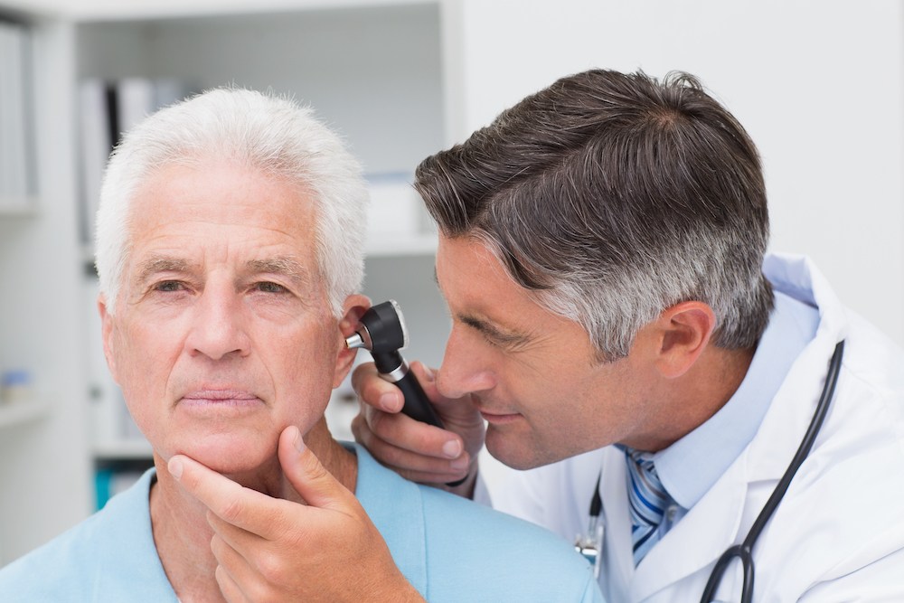glum looking man having his ear canal inspected by hearing specialist