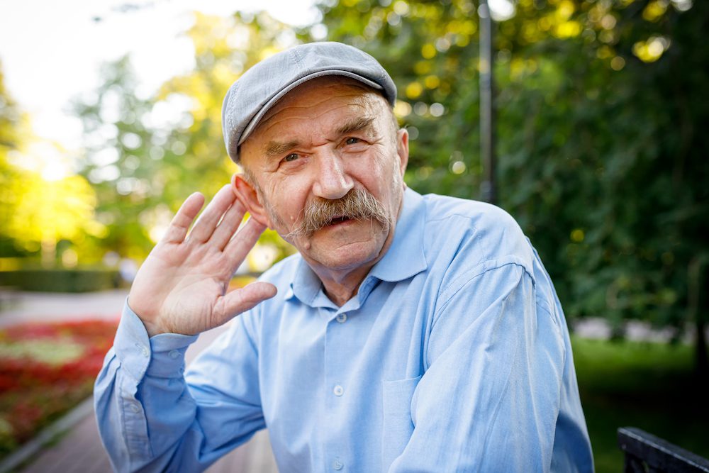 older gentleman gesturing towards his ear expressively